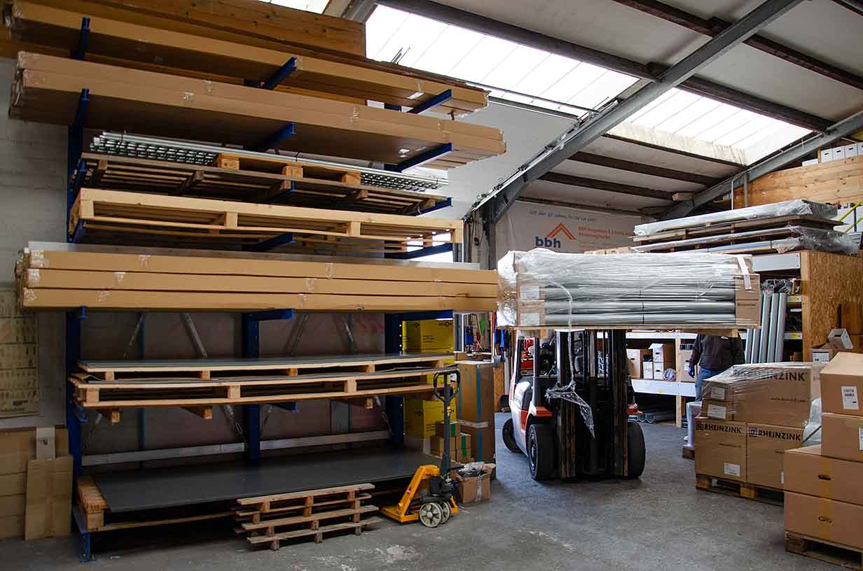 Gabelstapler hebt verpackte Metallrohre in Lager mit Holzpaletten und Kartons.