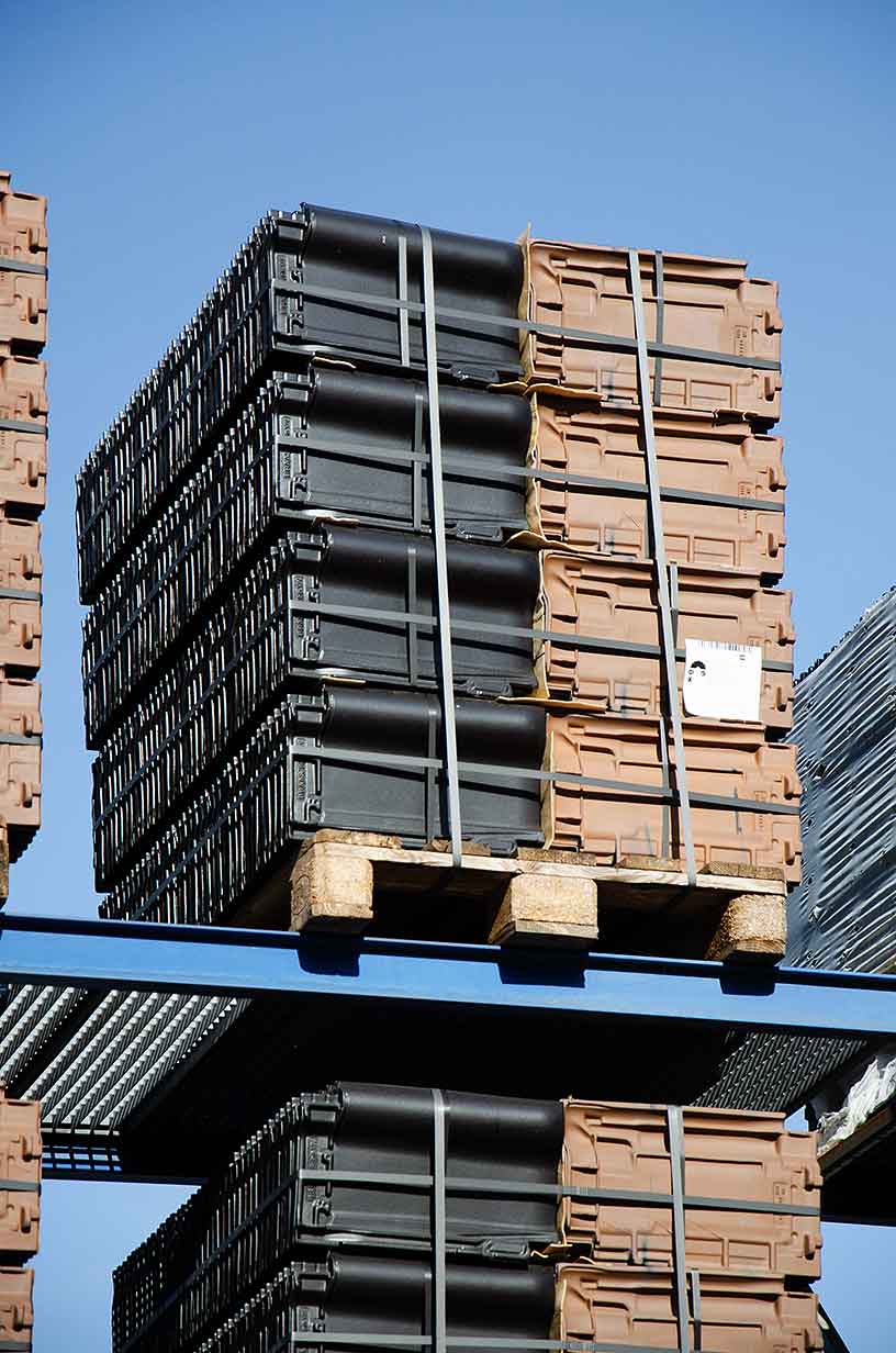 Auf einem Holzpaletten stapelweise braune und schwarze Plastikbehälter gesichert mit Gurtbändern im Freien.