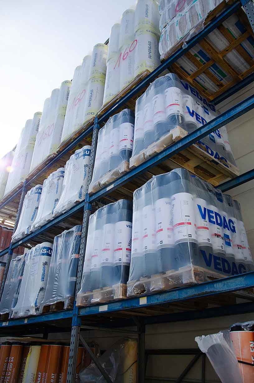 Regal mit als VEDAG verpackten Baumaterialrollen unter klarem Himmel.