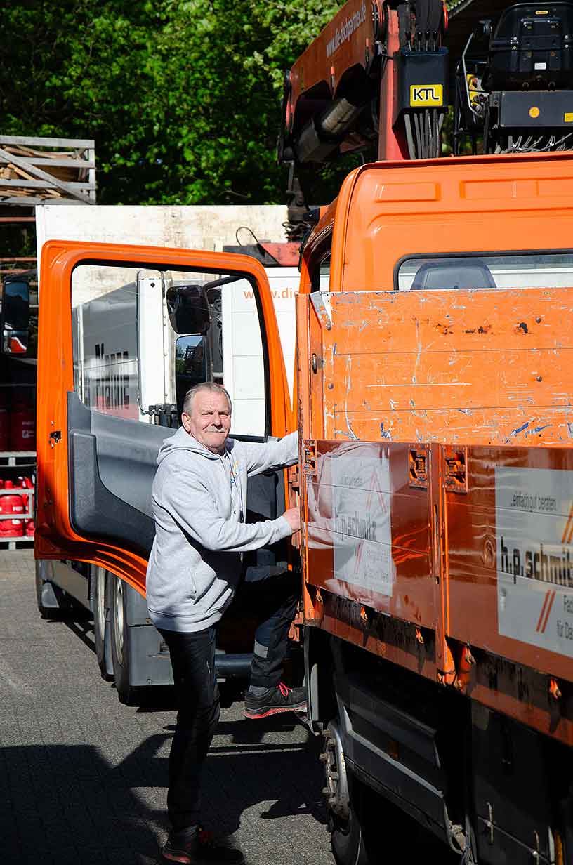 Mann steigt in orangefarbenen Lastwagen mit geöffnetem Fahrertür im Freien ein.