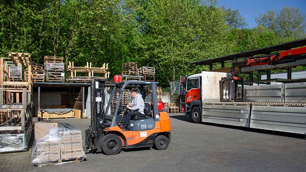 Gabelstapler hebt Paletten mit verpackten Rheinzink-Kartons vor LKW und Lagerplatz.