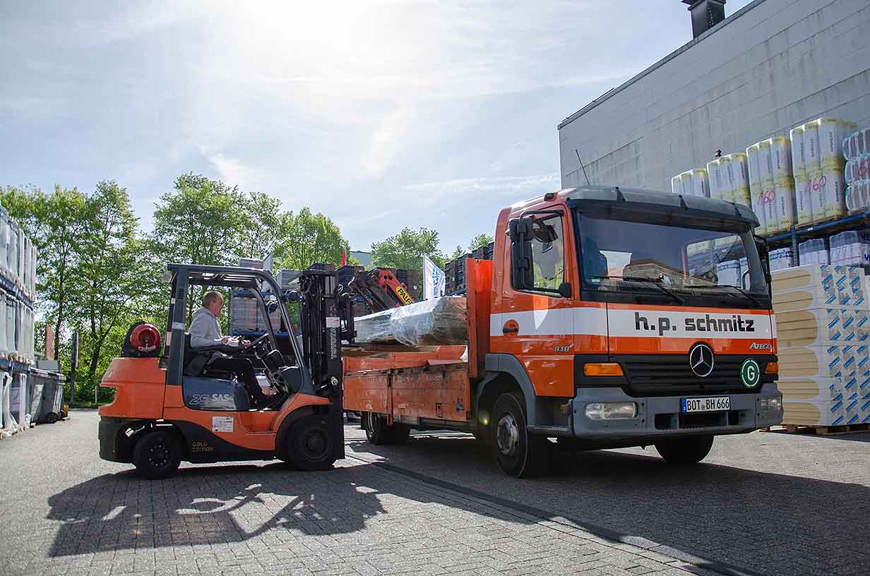 Gabelstapler lädt lange Ladung auf orangefarbigen Lastwagen von h.p. schmitz.