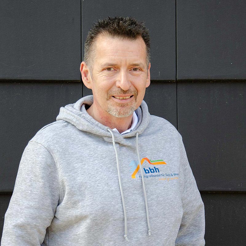 Mann mit grauem Hoodie vor schwarzer Wand, Hoodie hat bbh-Logo für Dach- und Wasserservice.