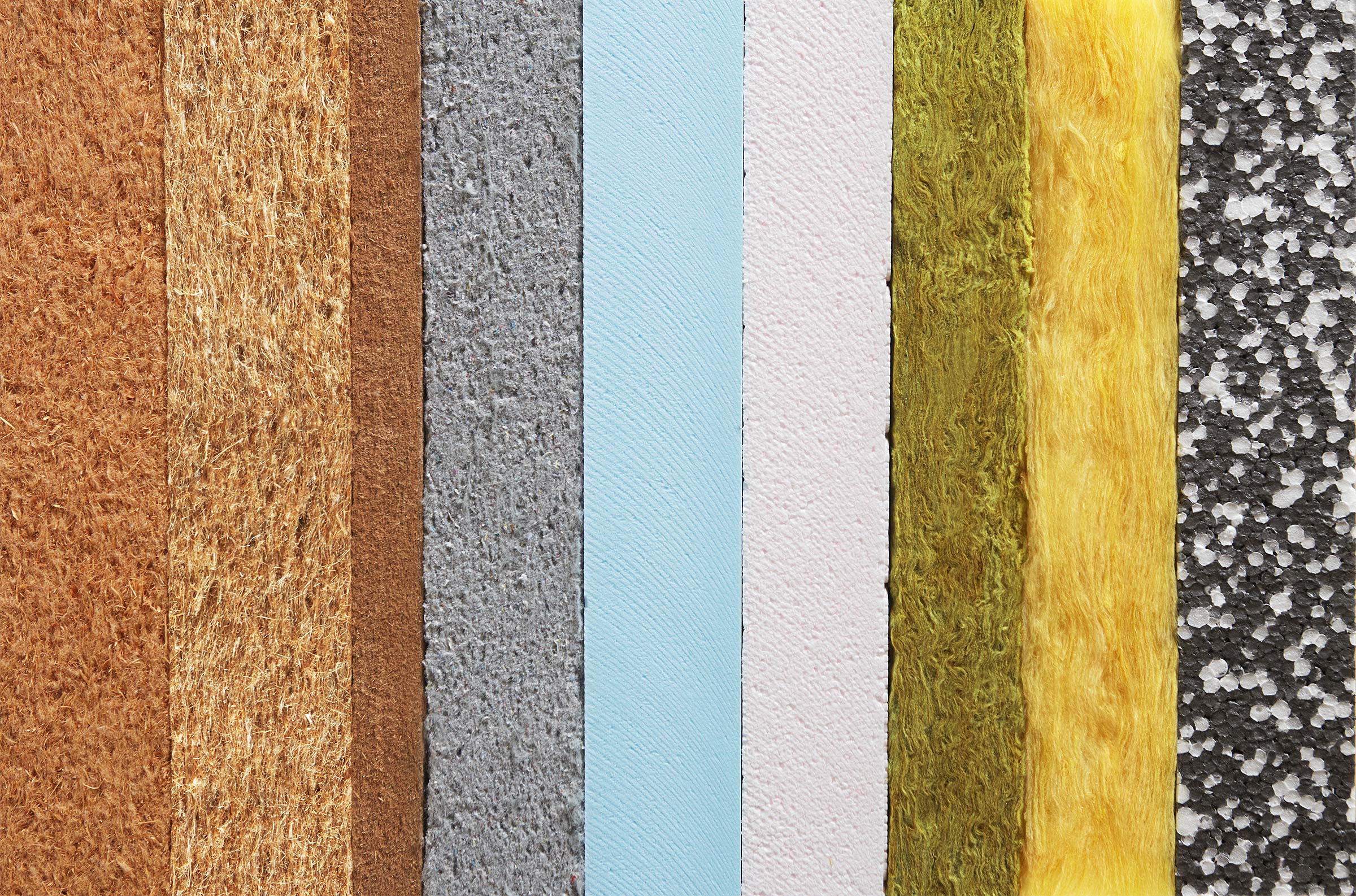 Verschiedene Dämmstoffe in vertikalen Streifen: braun, grau, blau, rosa, grün, gelb und schwarz-weiß.