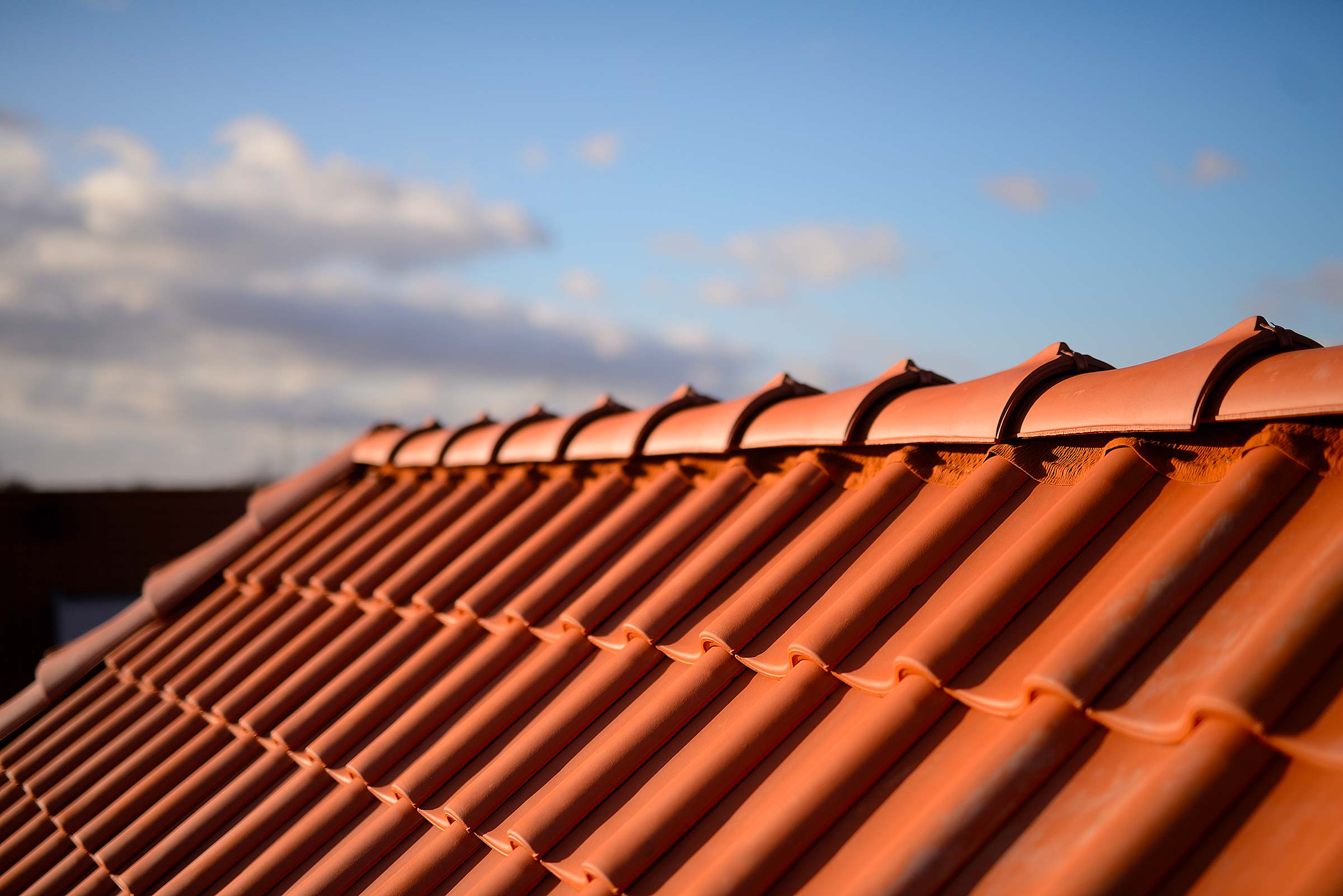 Nahaufnahme eines Dachs mit orangen Ziegeln unter klarem Himmel und vereinzelten Wolken.