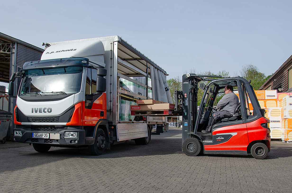 Ein Gabelstapler lädt Kartons auf einen Iveco-Lastwagen mit offener Seitenplane.