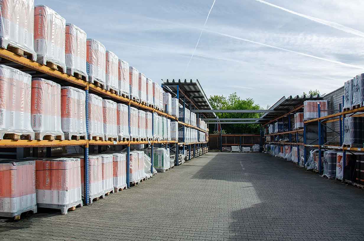 Lagerbereich mit Regalen voller in Folie verpackter Paletten unter bewölktem Himmel.