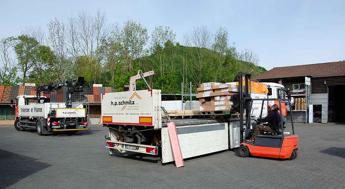 Stapler lädt palettierte Holzplatten auf einen LKW mit h.p. schmitz-Logo auf einem Hof.