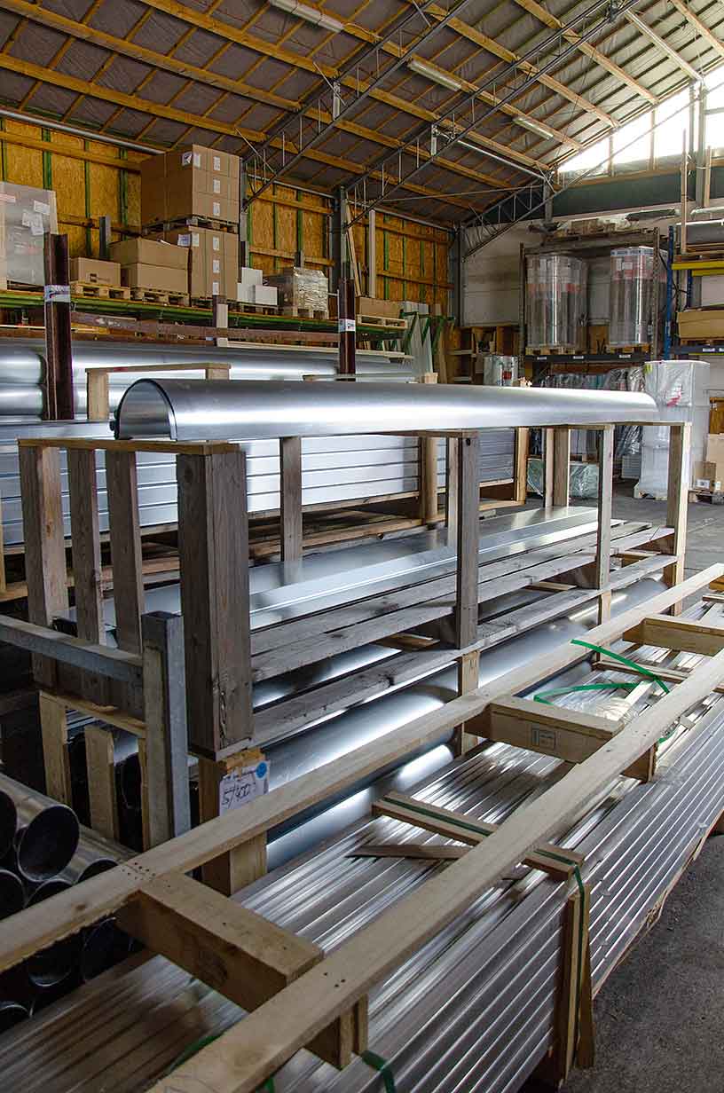 Lagerhalle mit Holzgestellen, die glänzende Metallrohre und -bleche lagern.