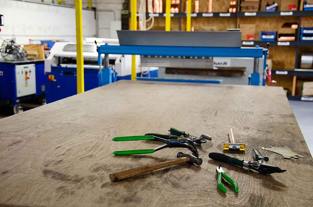 Verschiedene Werkzeuge mit grünen Griffen liegen auf einem großen Holztisch in einer Werkstatt.