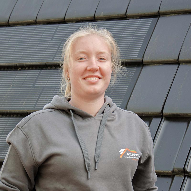 Lächelnde Frau in grauem Kapuzenpullover mit Firmenlogo vor Solarpaneelen.