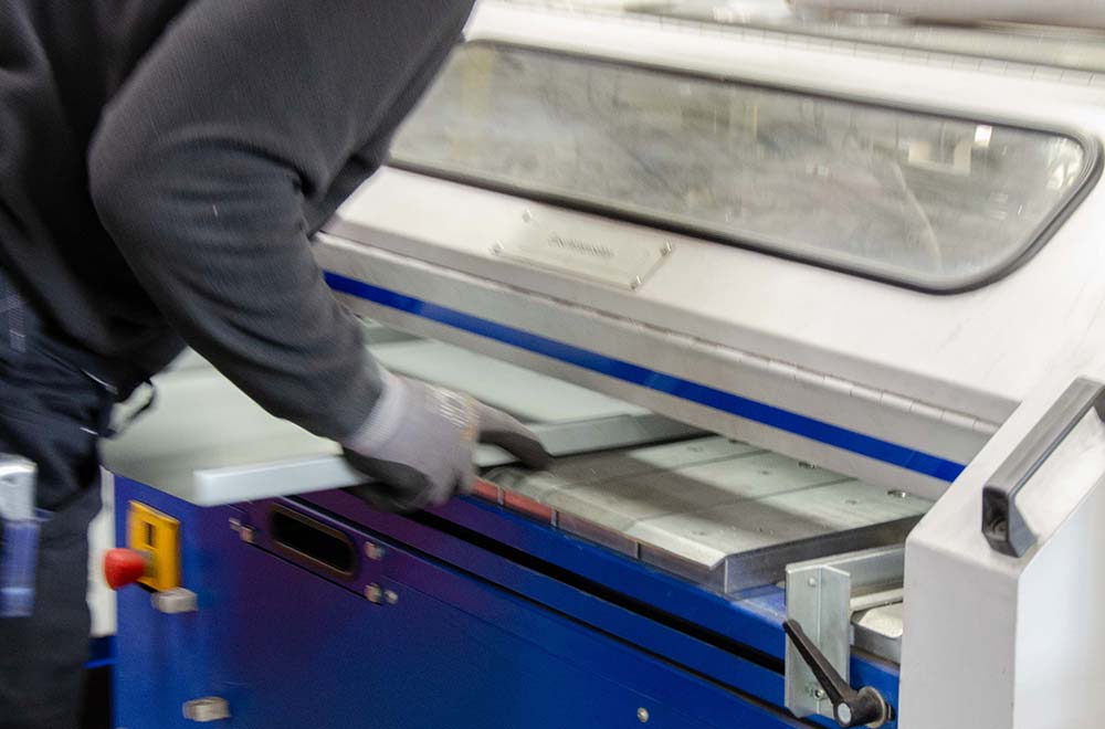 Person trägt graue Handschuhe und arbeitet an blauer Metallmaschine mit Hebel und Klappe.