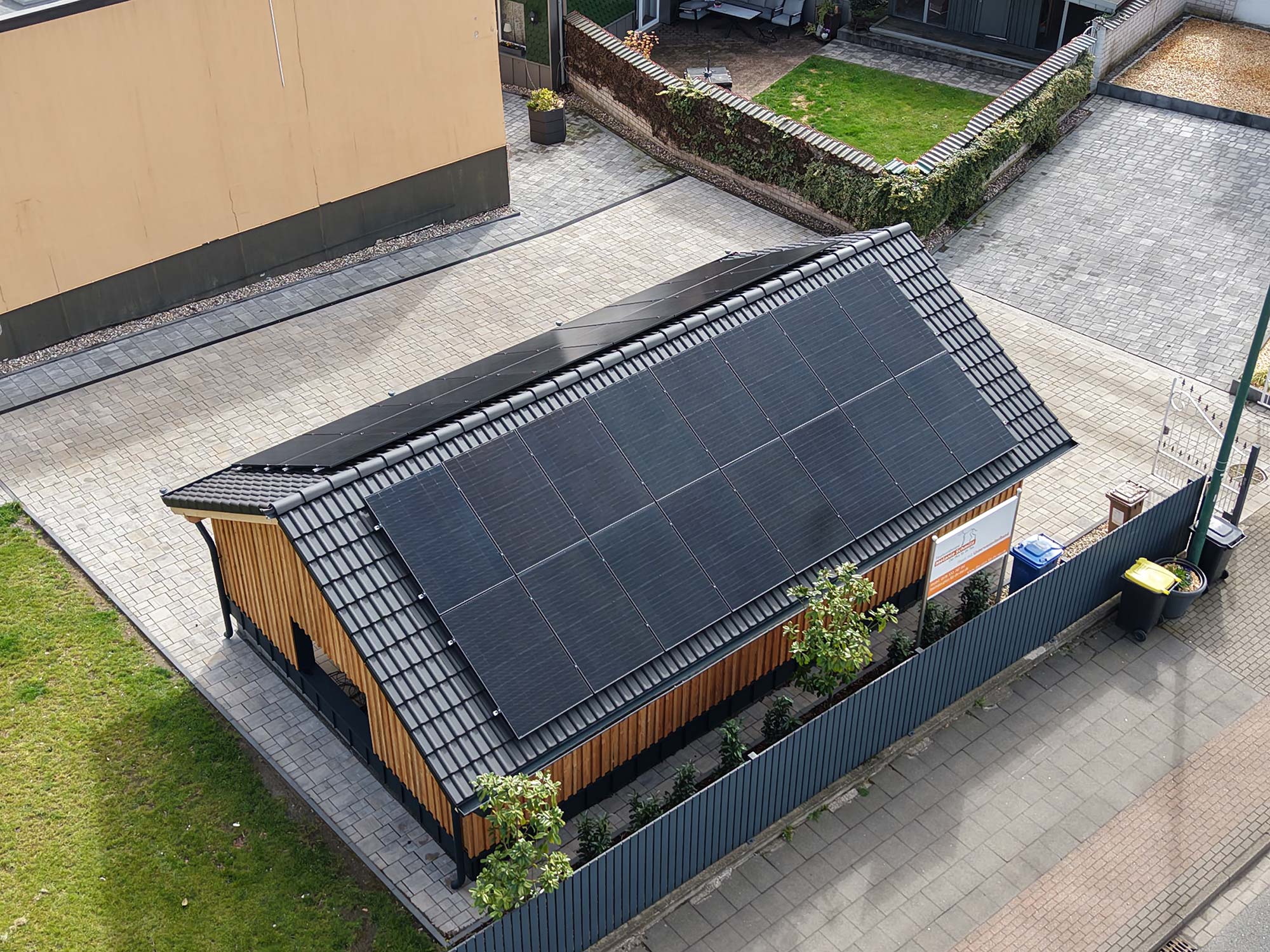 Haus mit schwarzem Dach, das vollständig mit Solarmodulen bedeckt ist, umgeben von Zaun und Grünfläche.