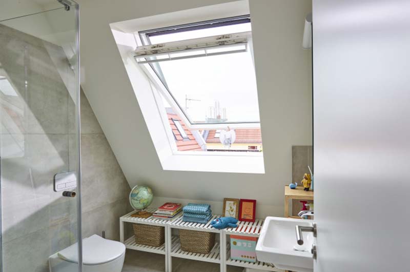 Helles Badezimmer mit großes Dachfenster, Toilette, Waschbecken und Regal mit Körben und Dekoration.