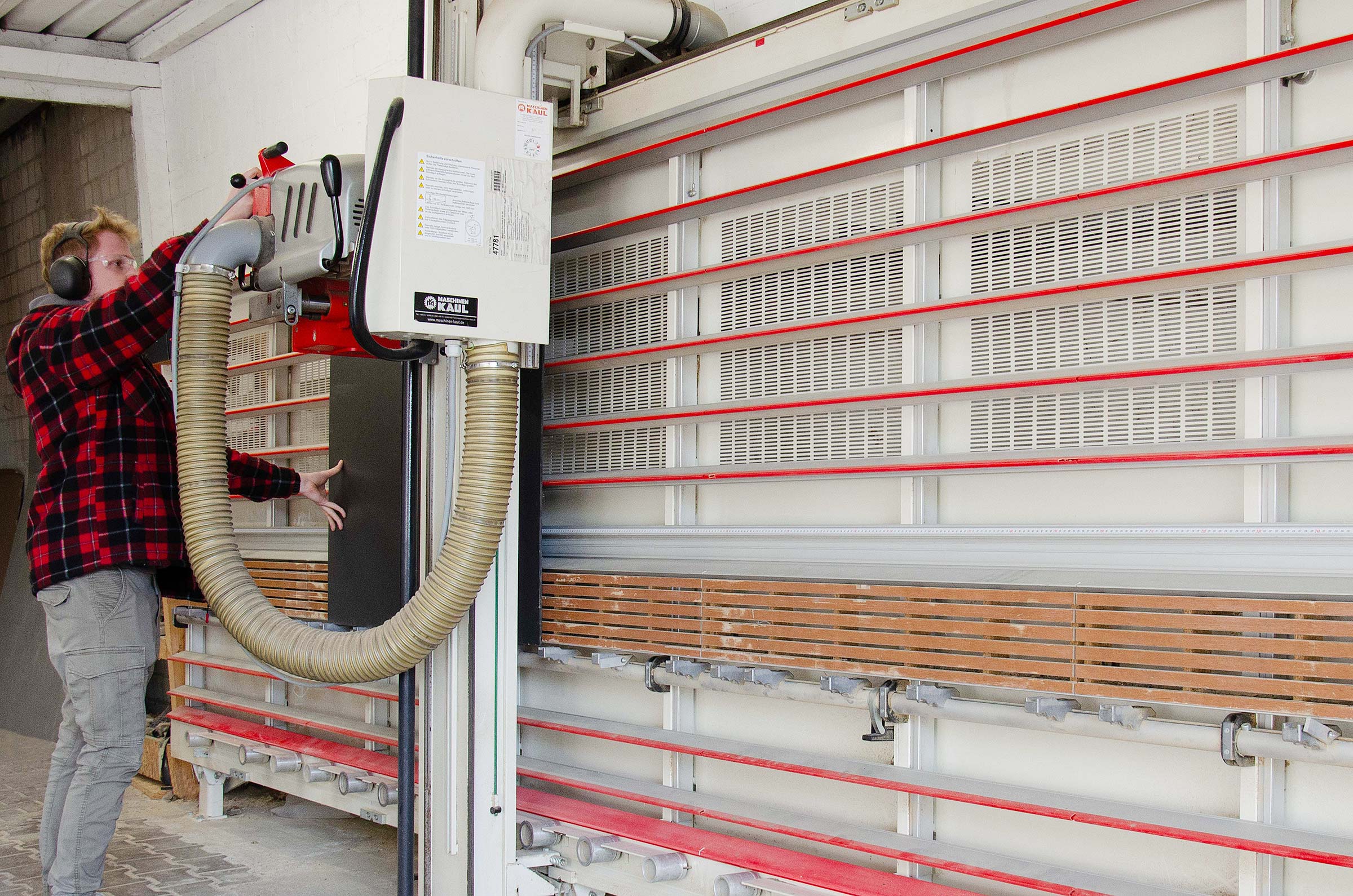 Person operating large industrial panel saw machine to cut wooden boards in workshop.
